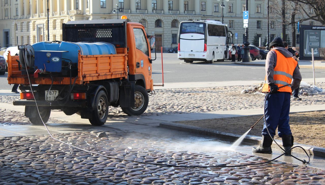about-01 A city worker uses a water hose to clean the urban streets in a sunlit scene.
