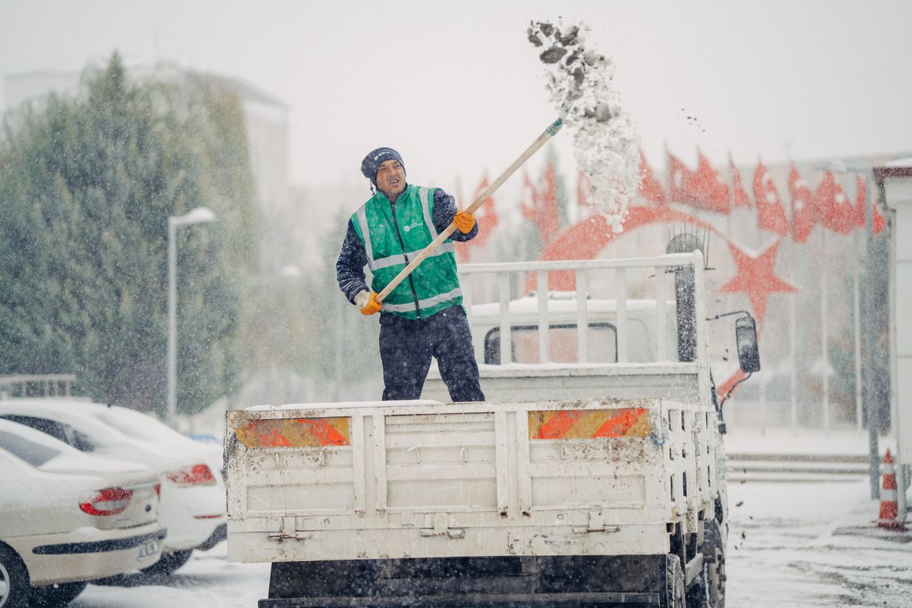 hero-img-01 A worker shovels snow off a truck during a snowy winter day, showcasing winter work effort.