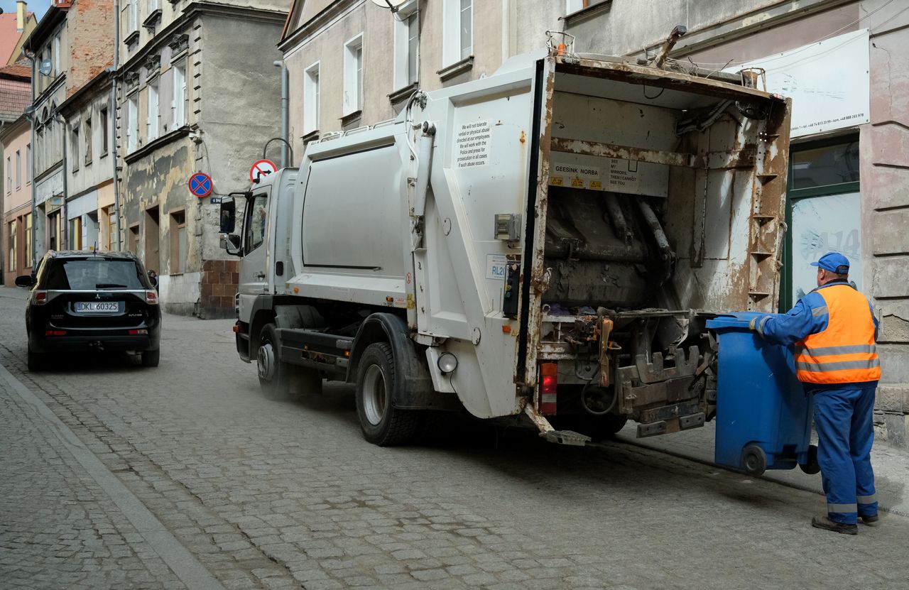 services-01 City street scene with garbage truck and worker handling waste bin.